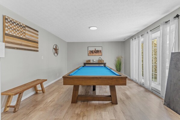 Une table de billard dans une pièce avec un banc en bois, une décoration en forme d’étoile et un tableau encadré au mur.