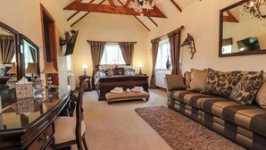 A spacious room with a large bed, a sofa, a desk with a chair, and a chandelier.