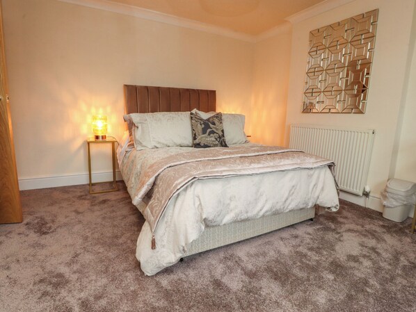 A bedroom with a bed, a bedside lamp, a radiator, and a decorative wall panel.