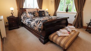 A bedroom with a large bed, a nightstand, a lamp, a window with curtains, and a radiator.
