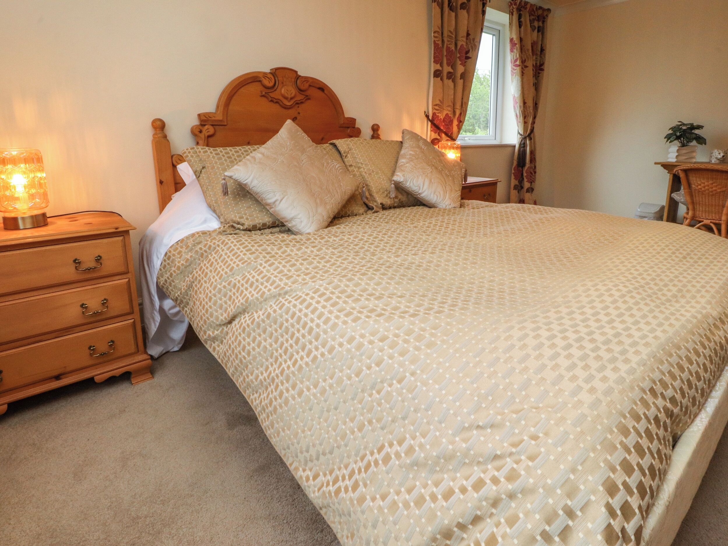 A bedroom with a wooden headboard, a patterned bedspread, and a bedside table with drawers.