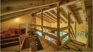 Ein gemütliches Dachzimmer mit Holzbalken, einem roten Blumensofa und Blick ins Untergeschoss.