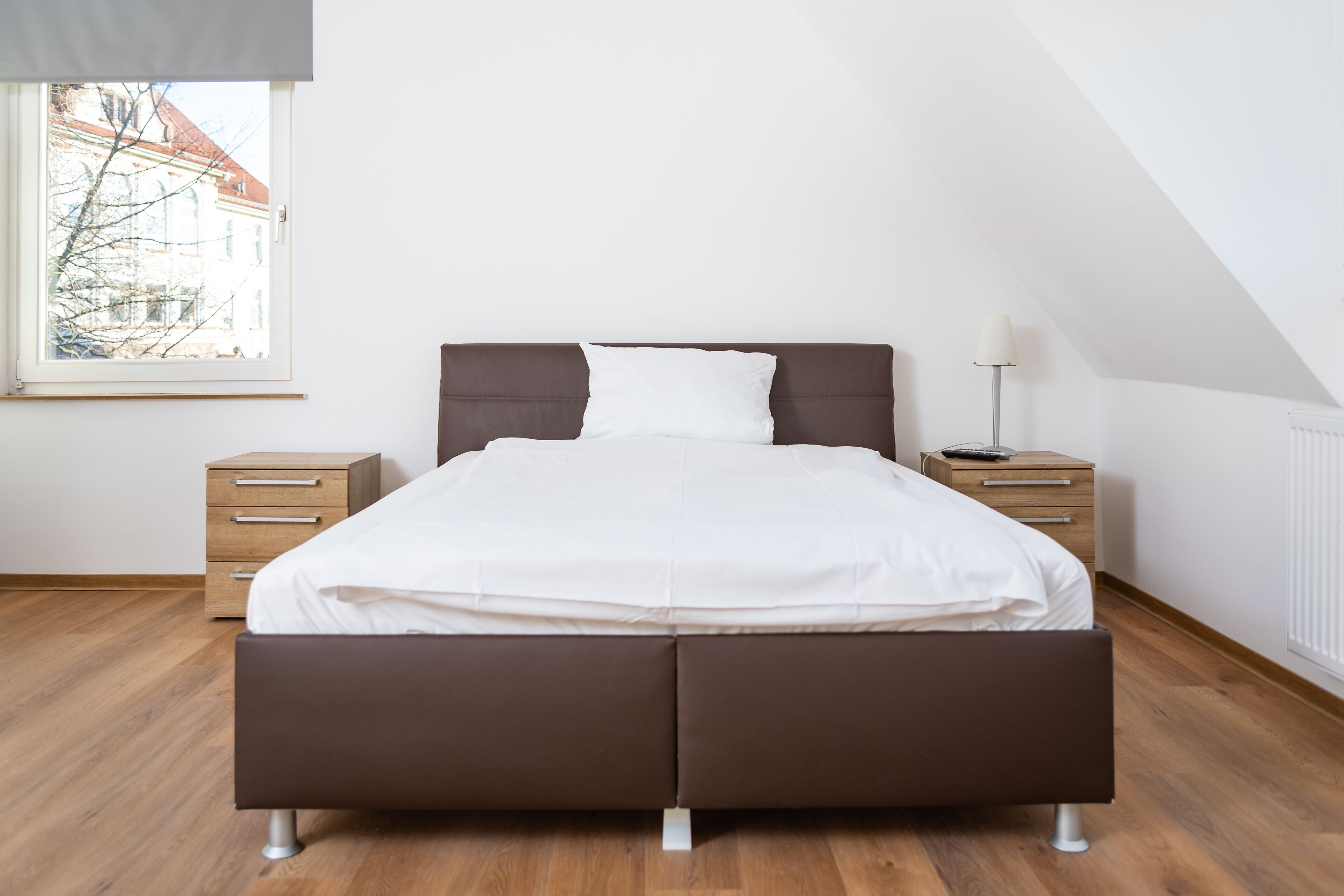 Un dormitorio moderno con una cama grande, cajones de madera, una mesita de noche y una lámpara.