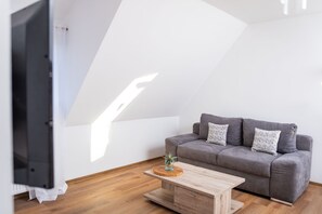 A modern living room with a grey sofa, a wooden coffee table, and a TV on a stand.