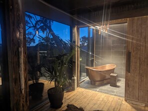Een moderne badkamer met een vrijstaand bad, grote ramen en een potplant.