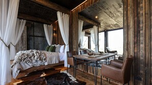 Une chambre à coucher au style rustique, avec un lit en bois, des rideaux blancs, un plaid en fourrure et un tapis en peau de vache.