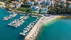 An aerial view of a marina with numerous boats docked, a sandy beach, and surrounding residential buildings. - Beachfront Villa Naviblue with Pool (Pula)