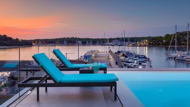A poolside area with lounge chairs and a view of a marina during sunset. - Beachfront Villa Naviblue with Pool (Pula)