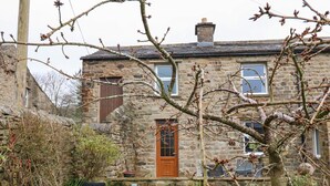 A stone house with a wooden door, a stone chimney, and a garden with various plants and a lawn. - Stoneleigh Cottage (Richmond)