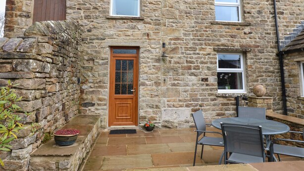 A stone house with a wooden door, two windows, and a patio with a table and chairs. - Stoneleigh Cottage (Richmond)