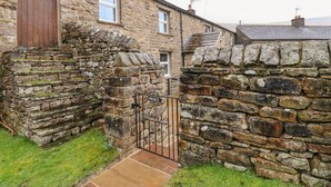 A stone house with a wooden door, a small window, and a stone wall with a gate. - Stoneleigh Cottage (Richmond)