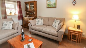 A cozy living room with a sofa, a wooden cabinet, a painting, and a clock on the wall. - Stoneleigh Cottage (Richmond)