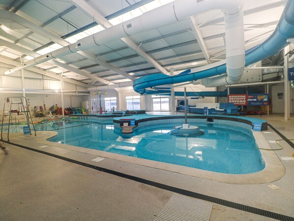 An indoor swimming pool with a blue slide, depth markers, and a lifeguard stand.
