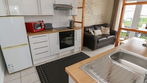 A compact kitchen with white cabinets, a red microwave, a black oven, and a wooden countertop. - Shipwreck Chalet (Kidwelly)