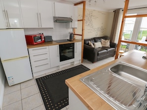 Una cocina compacta con gabinetes blancos, un microondas rojo, un horno negro y una encimera de madera.