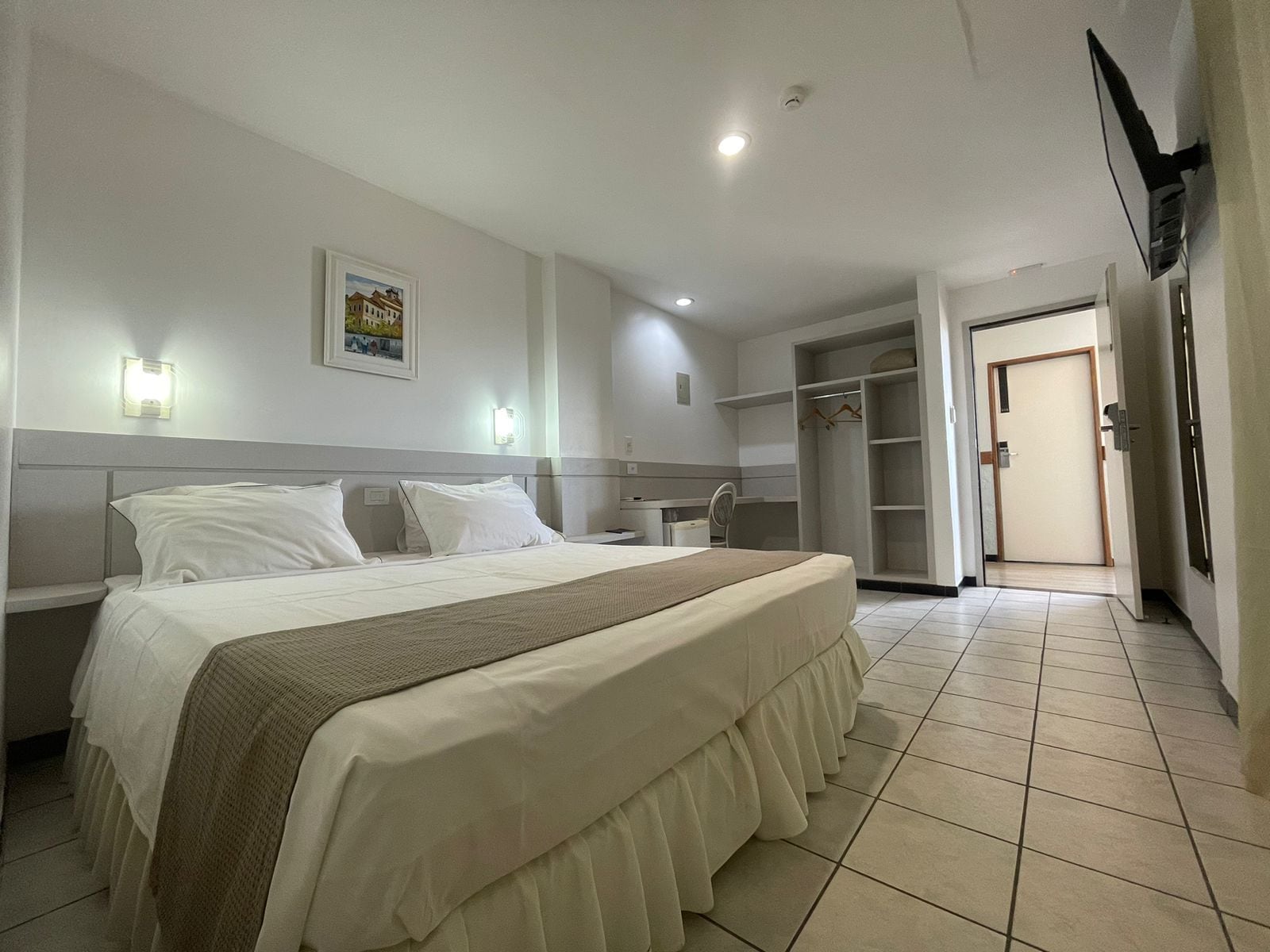 Una habitación de hotel con una cama, mesita de noche, armario y una puerta que da a otra habitación.