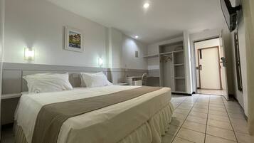 Una habitación de hotel con una cama, mesita de noche, armario y una puerta que da a otra habitación.