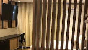 Un salon moderne avec un plancher en bois, un canapé, un téléviseur fixé au mur et un rideau servant de séparation.