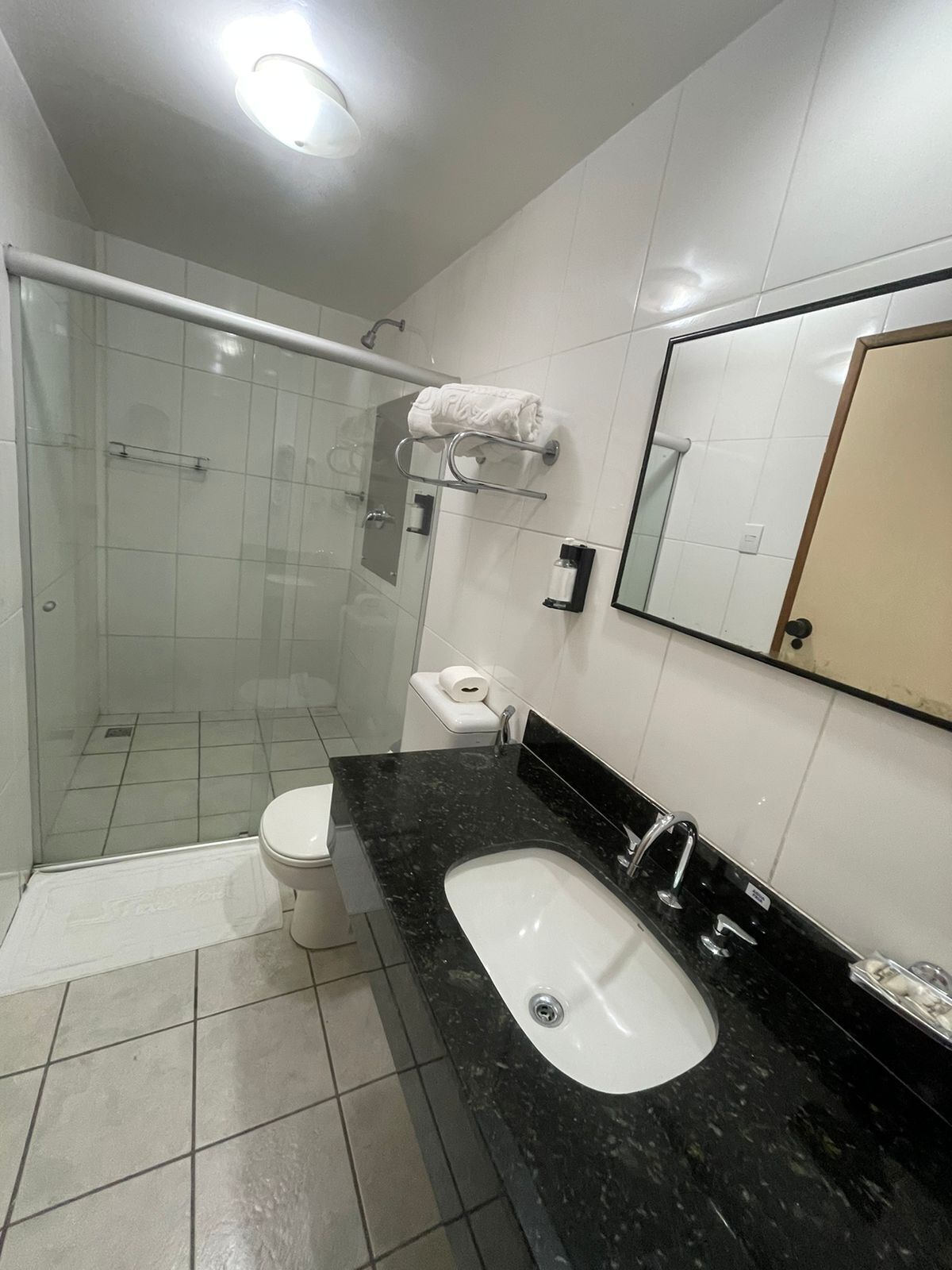 Un baño moderno con ducha envuelta en vidrio, inodoro blanco, lavamanos de mármol negro y un espejo grande.