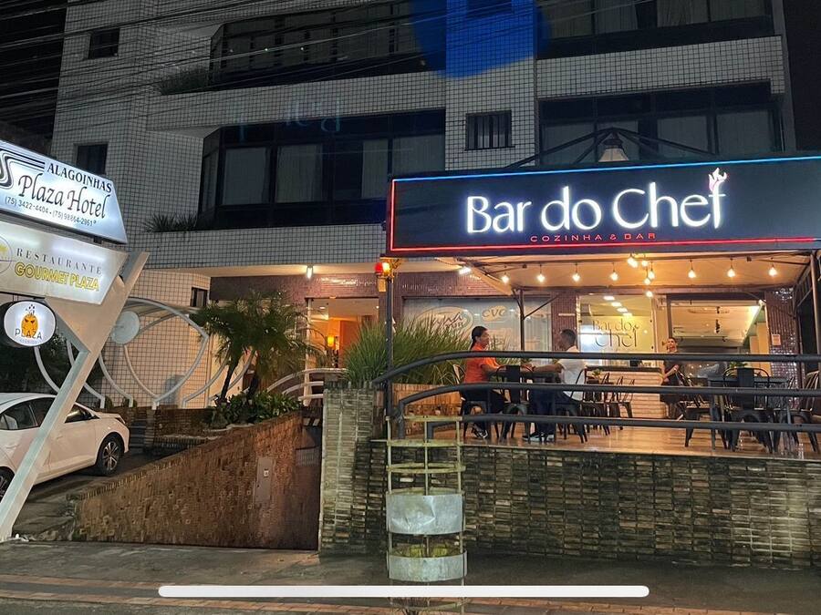 En restaurant kaldet Bar do Chef med udendørs siddepladser og et skilt for Alagoinhas Plaza Hotel i baggrunden.