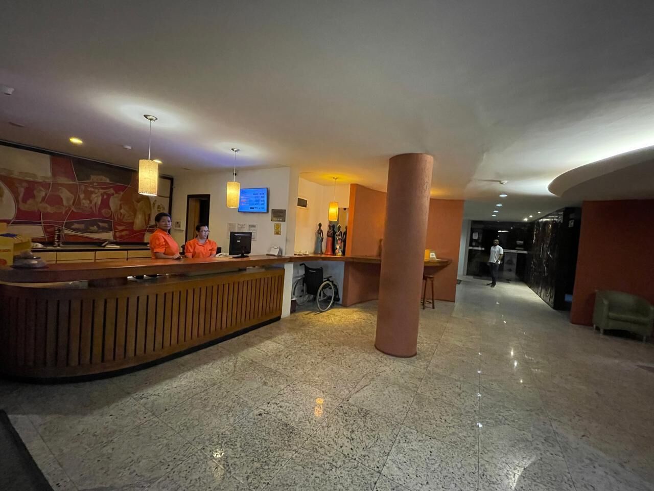 A hotel lobby with a reception desk, a large pillar, and a wheelchair.