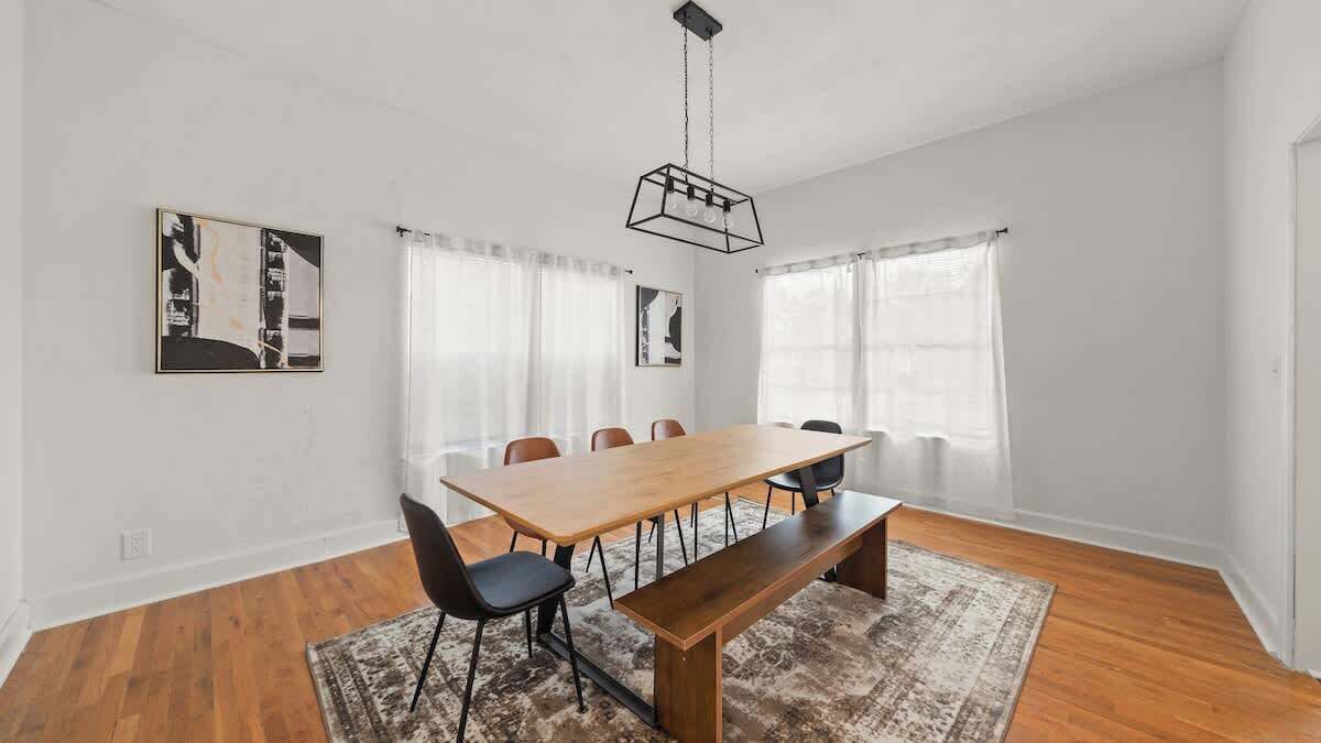 A modern room with a wooden dining table, black chairs, a bench, and a patterned rug.