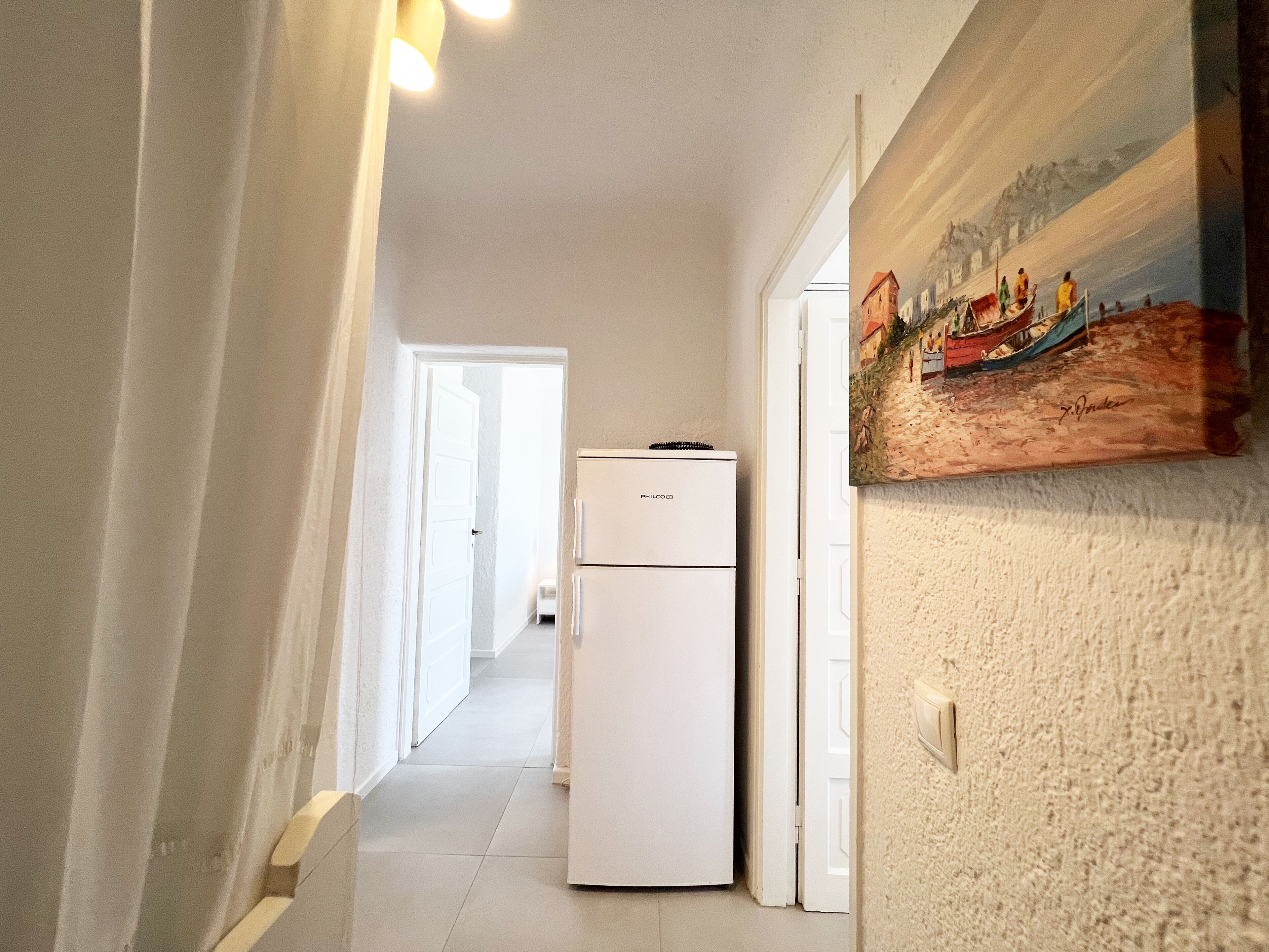 Ein Flur mit einem weißen Kühlschrank, einer Tür zu einem anderen Raum und einem Bild an der Wand.