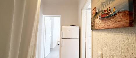 A hallway with a white refrigerator, a door leading to another room, and a painting on the wall.
