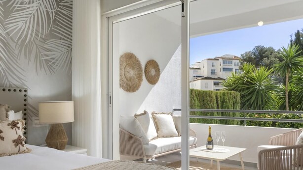 A bedroom with a bed, bedside lamp, and a view of a balcony with a sofa, chairs, and a table. - Apartment in Medina Garden for 4 people | 201 (Puerto Banús - Marbella)