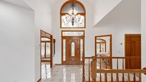 Um corredor amplo com escada de madeira, um candelabro e um grande arco de janela.