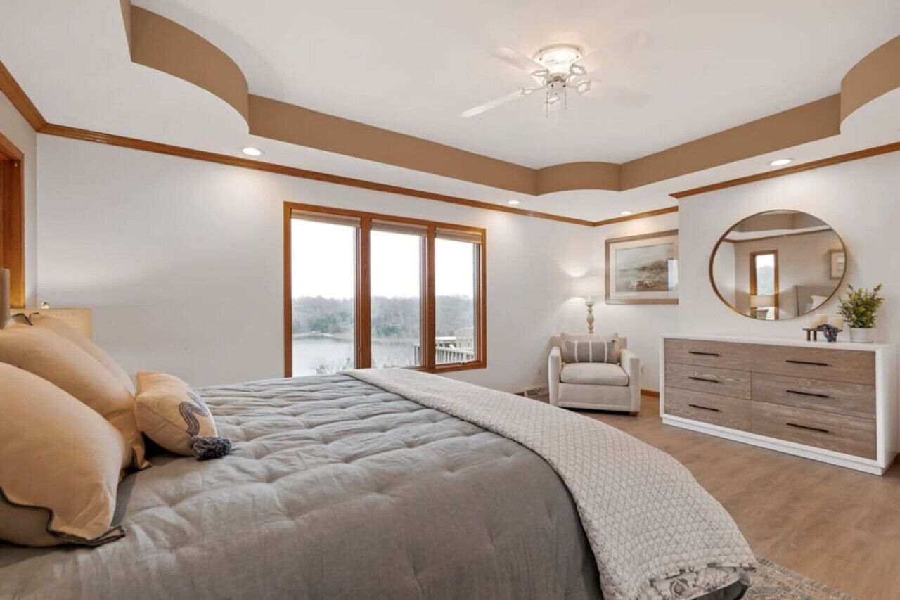 Un dormitorio con cama, cómoda, silla, espejo y ventana con vistas.