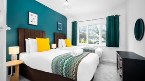 Ett hotellrum med två sängar, turkosa väggar, ett fönster med gardiner och en svart byrå.