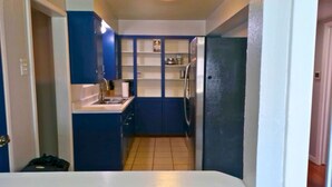 Una cocina compacta con armarios azules, una encimera blanca y un refrigerador.