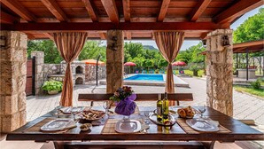An outdoor dining area with a pool view, stone walls, and a wooden pergola.