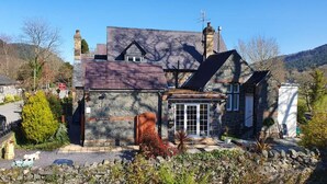 A stone house with a sloped roof, a small attached garage, and a front door with a glass panel. - Chambers Apartment @ The Old Magistrates (Betws-Y-Coed)