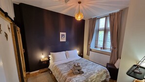 A bedroom with a bed, bedside lamps, a radiator, a window with curtains, and a hanging light fixture. - Chambers Apartment @ The Old Magistrates (Betws-Y-Coed)