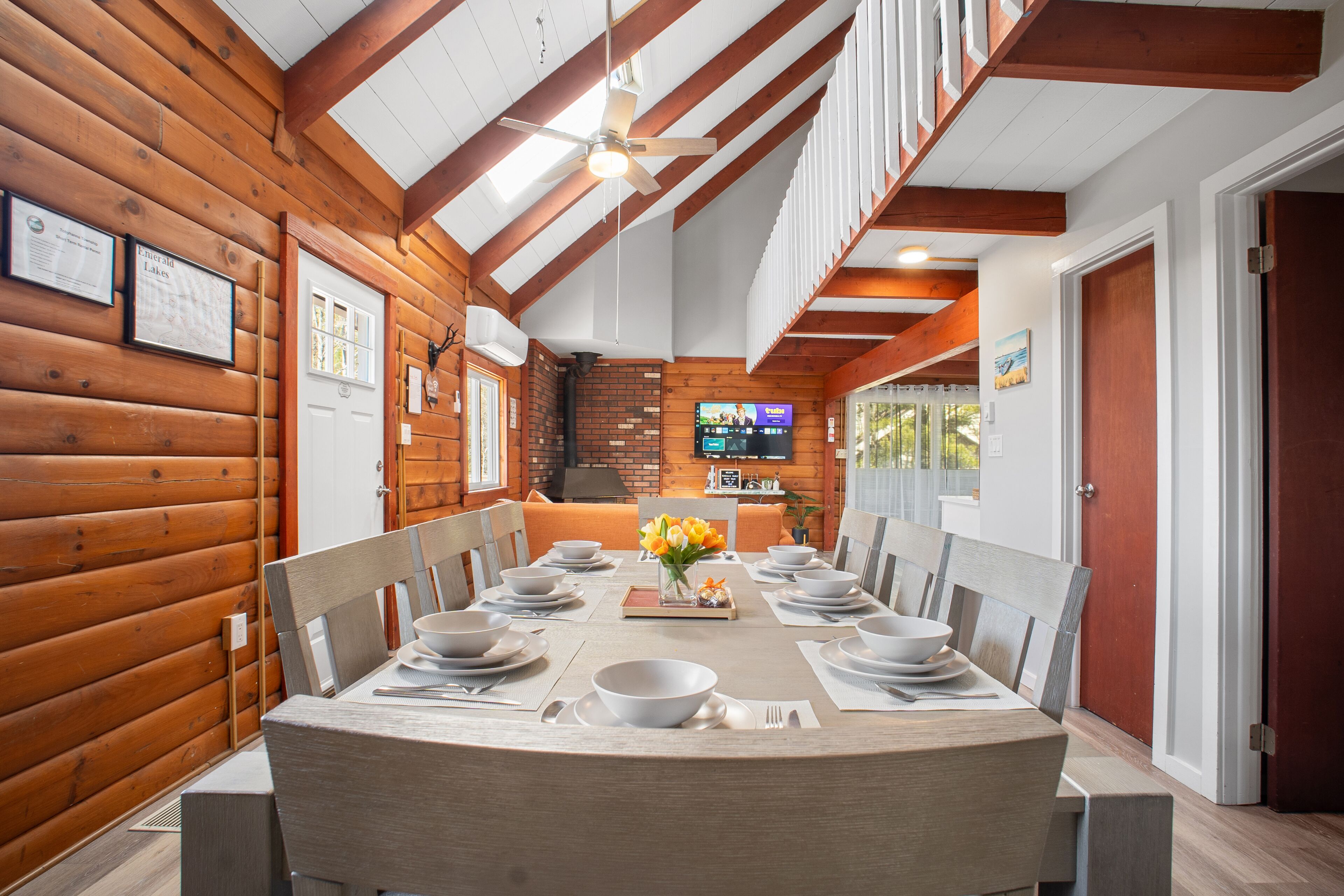 A dining area with a long wooden table set for a meal, wooden walls, and a TV mounted on the wall.