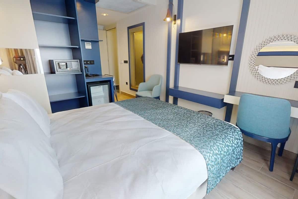 A hotel room with a large bed, a desk, a chair, a TV, and a minibar.