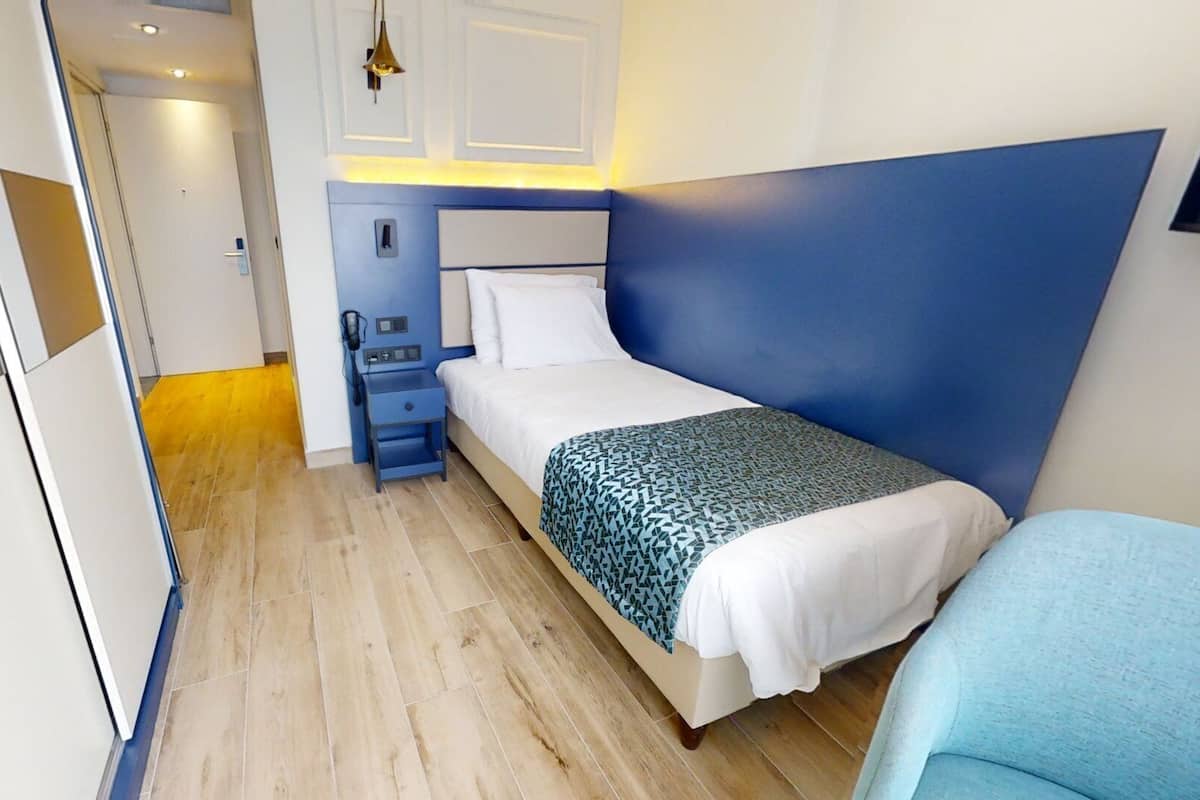 A compact hotel room with a bed, bedside table, and a small seating area.