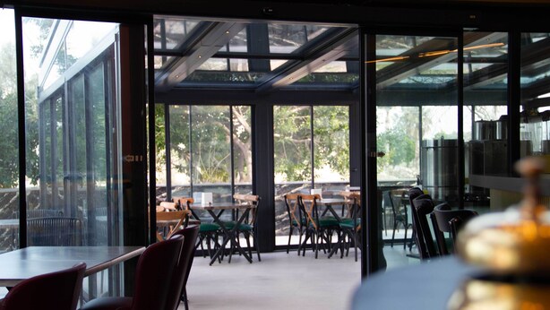 Un comedor interior con paredes de vidrio, mesas y sillas.