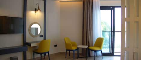 A hotel room with a bed, a desk, two chairs, a TV, and a large window with curtains.