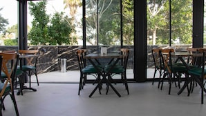Un comedor interior con mesas y sillas, ventanas amplias que dan a árboles, y una pared de mármol.
