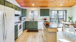 Eine moderne Küche mit grünen Schränken, einem weißen Kühlschrank und einer Holzbalkendecke.