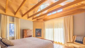 Une chambre confortable avec un grand lit, des poutres en bois, une cheminée et une fenêtre avec des rideaux.