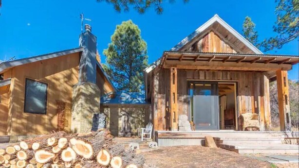Une cabane rustique dotée d’une cheminée, d’une grande fenêtre et d’un porche avec une chaise.