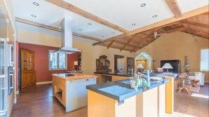 Une cuisine spacieuse dotée d’un grand îlot central, de poutres apparentes au plafond et d’un coin repas avec une table et des chaises.