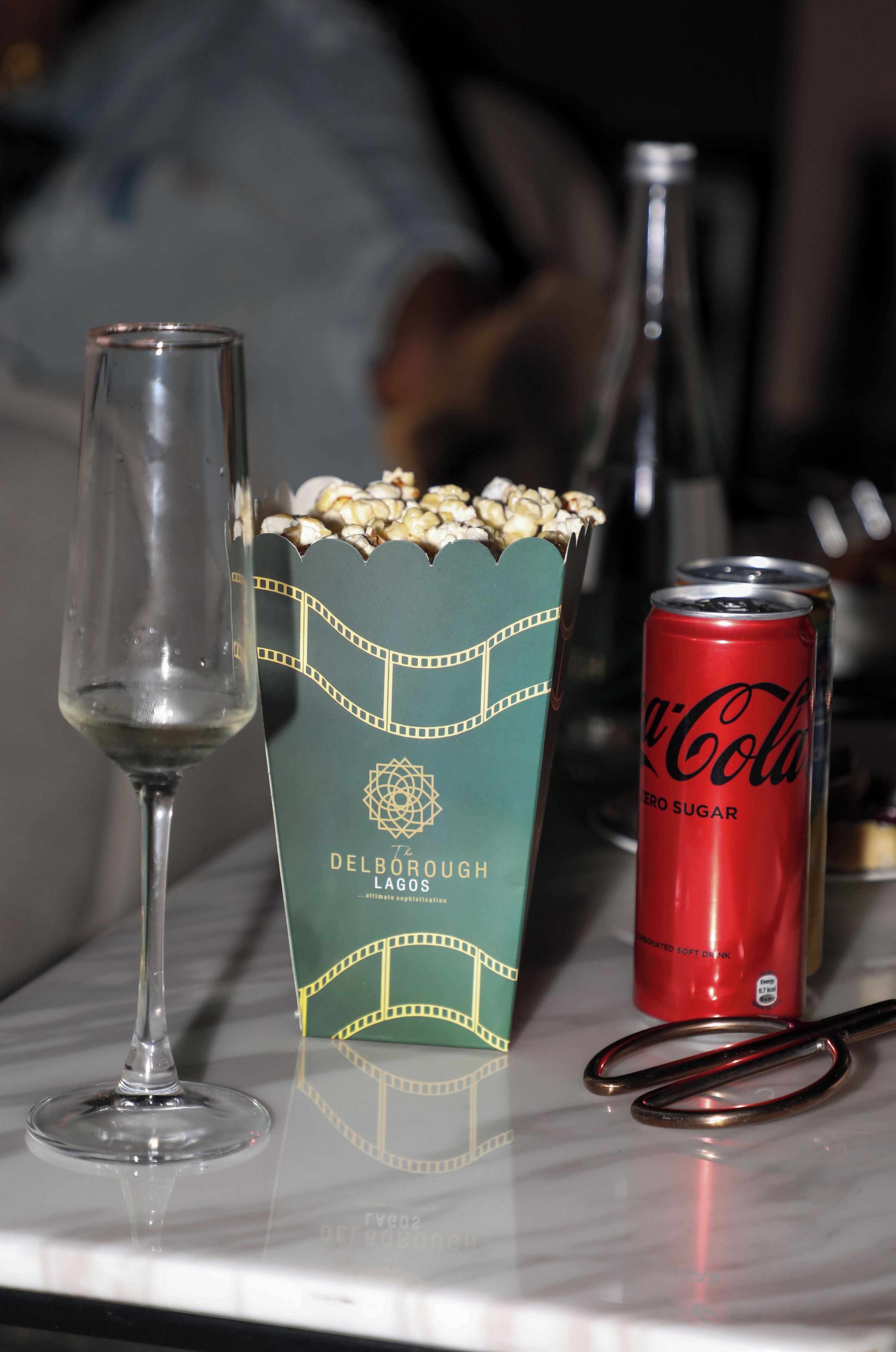 A table with a wine glass, a box of popcorn, a can of Coca-Cola, and a pair of glasses.