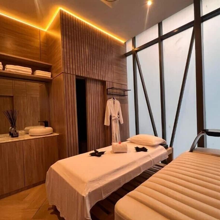 A modern spa room with a wooden vanity, a massage table, and a large window.