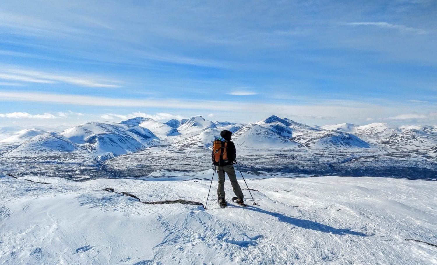 Iemand staat op een besneeuwde berg met een helder uitzicht op verre bergen.