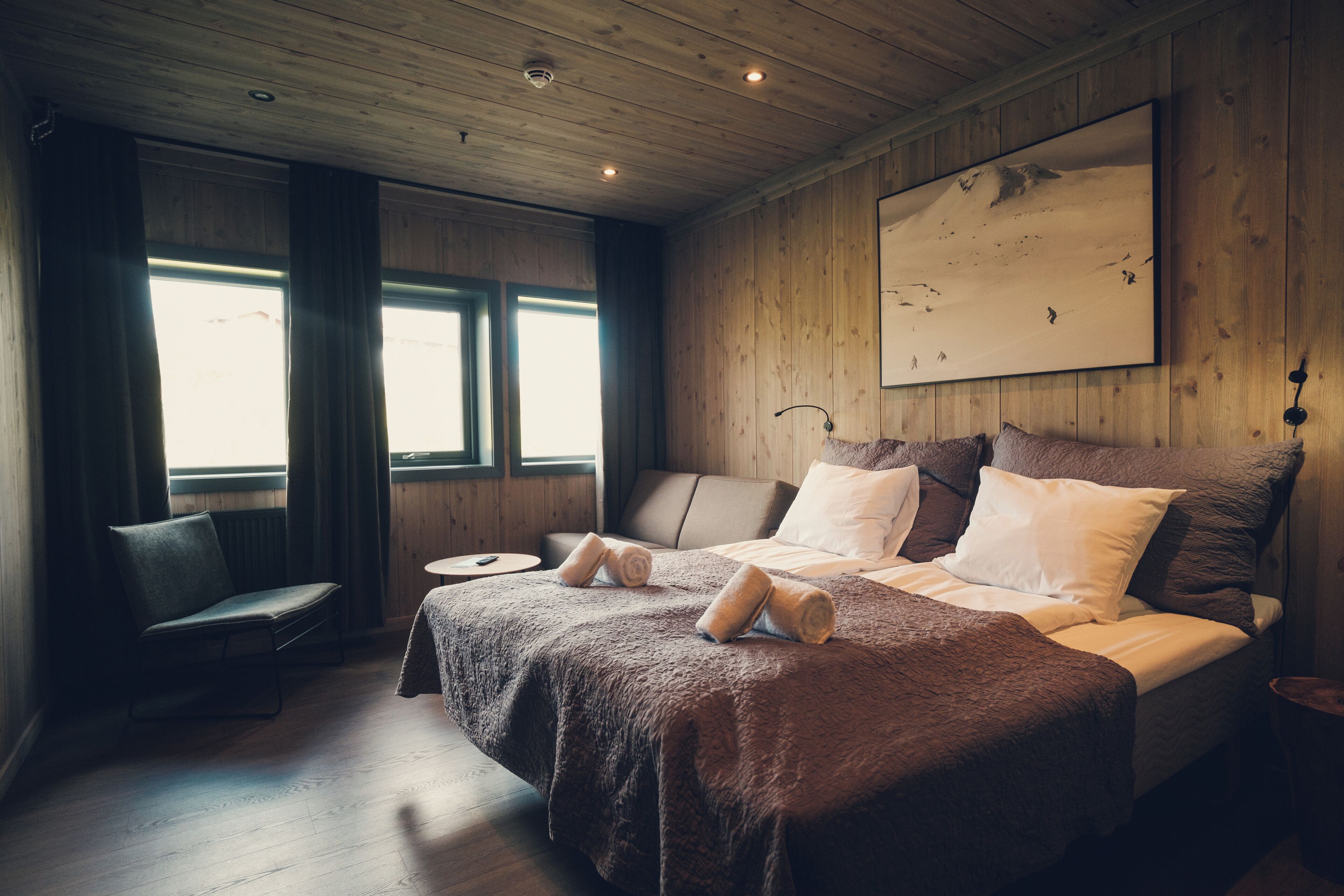 A wooden-paneled bedroom with a bed, a chair, and a painting on the wall.